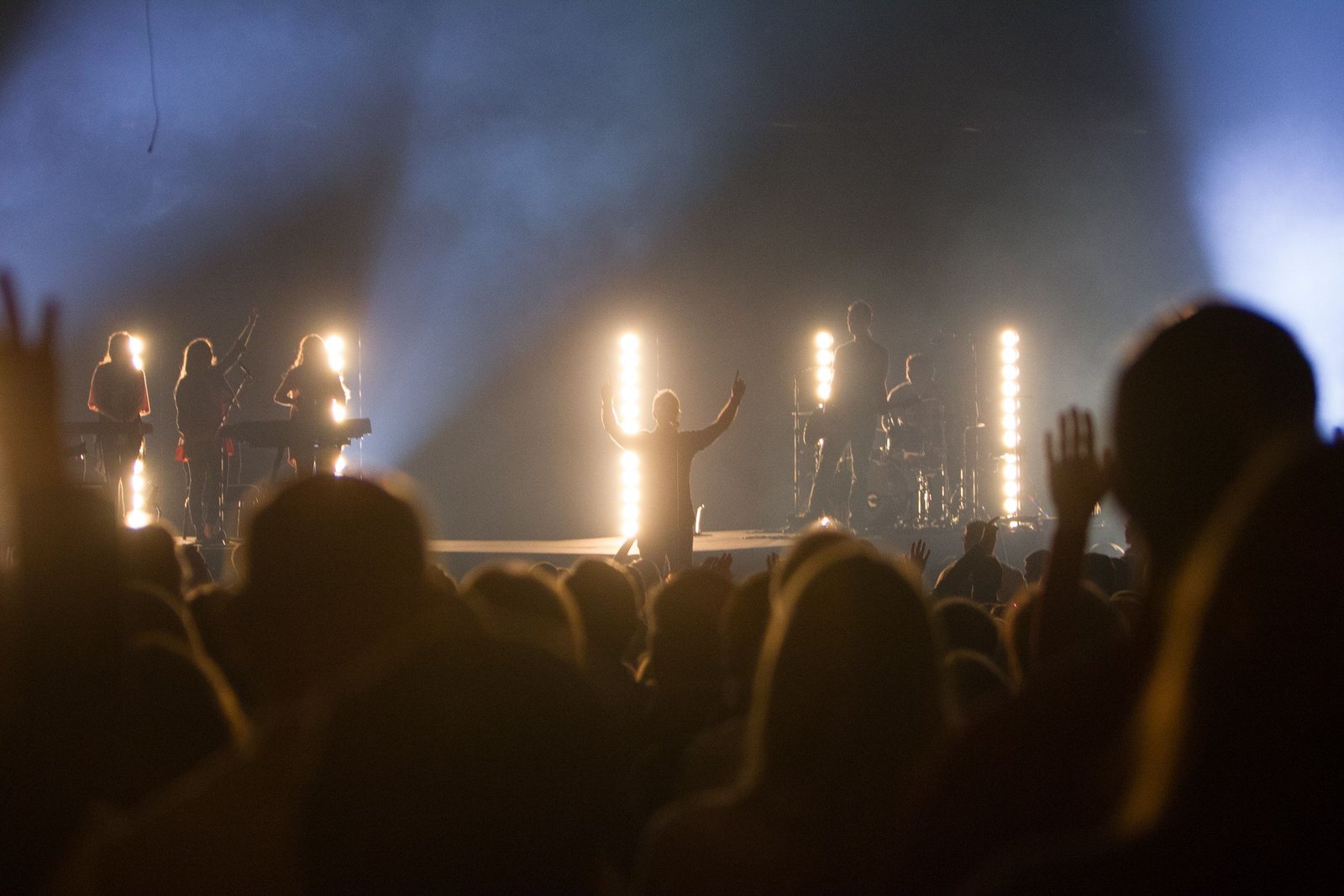 Vibrant live music concert with silhouetted band and cheering crowd under bright stage lights.